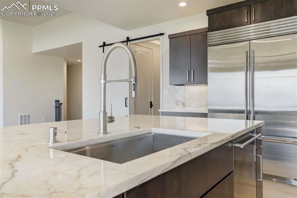 Image 11 of 34: Kitchen featuring dark brown cabinetry, light stone counters, stainless ste