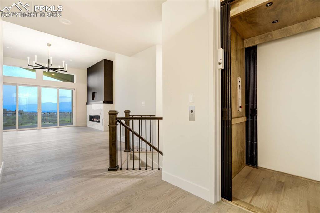 Image 12 of 34: Corridor featuring light wood-style flooring, elevator, an upstairs landing