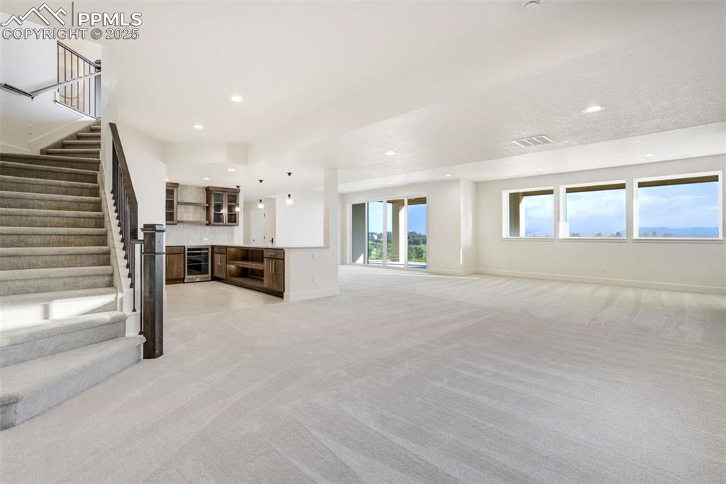 Image 21 of 34: Unfurnished living room featuring light carpet, stairway, wine cooler, and