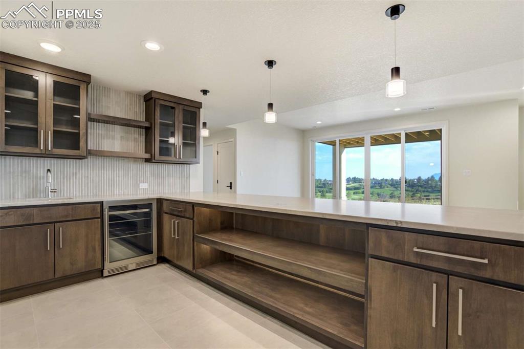 Image 23 of 34: Kitchen with open shelves, wine cooler, dark brown cabinets, decorative lig