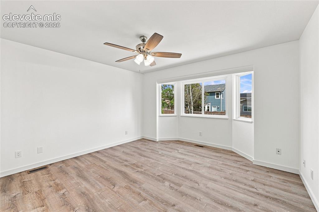 Image 14 of 30: Wood-finish flooring with a ceiling fan and a multi-pane bay window