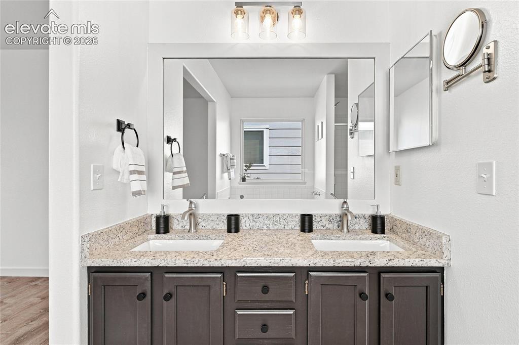 Image 17 of 30: Dual basin vanity with a speckled countertop, dark wood-finish cabinetry, a