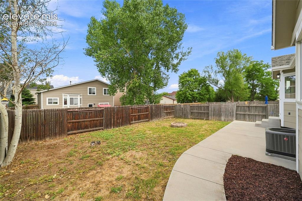 Image 24 of 30: Fenced backyard featuring a concrete patio, a fire pit, and mature trees