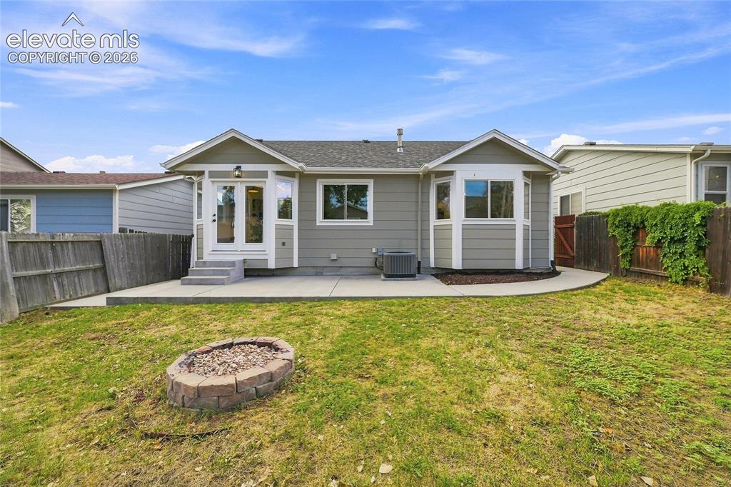 Image 25 of 30: Spacious backyard with a concrete patio, built-in fire pit, and privacy fen