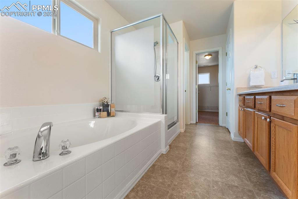 Image 18 of 50: Bathroom with vanity, a stall shower, a garden tub, dark tile patterned flo