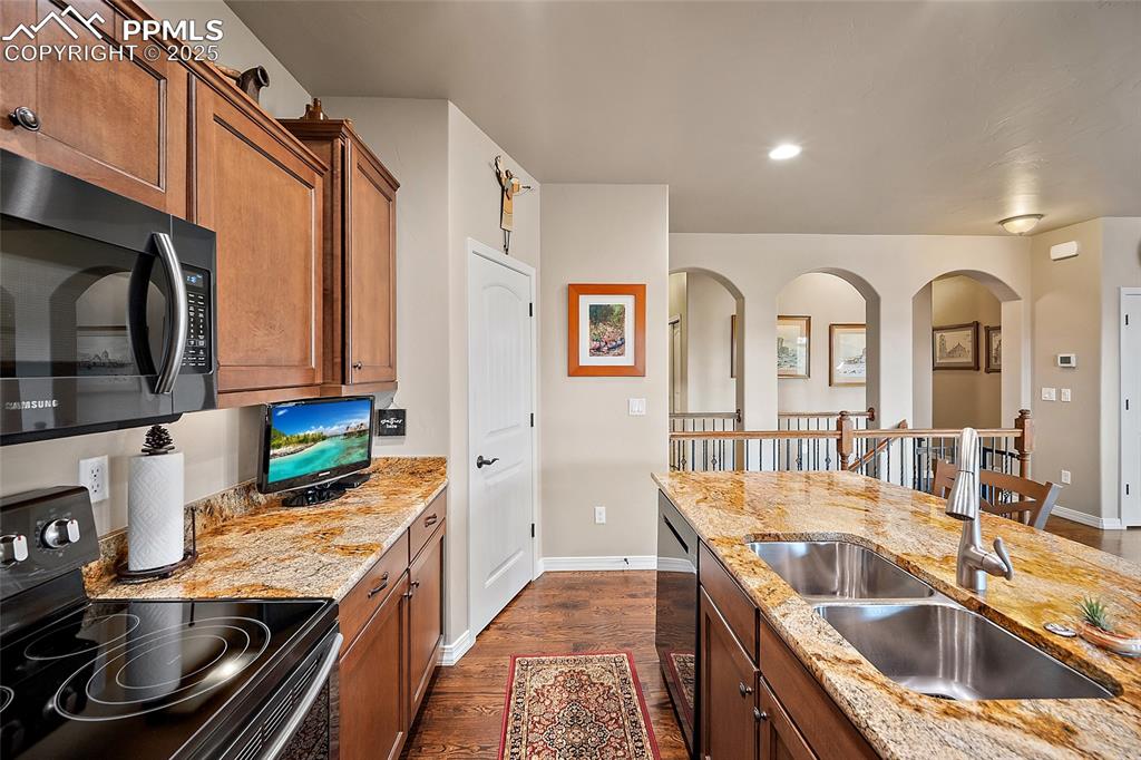 Image 13 of 39: Kitchen with black / electric stove, brown cabinetry, dark wood-style floor