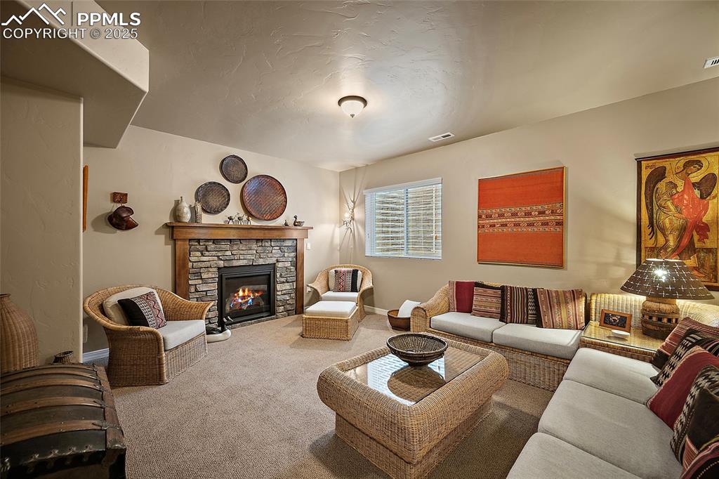 Image 23 of 39: Living area featuring a stone fireplace, carpet flooring, and a textured ce
