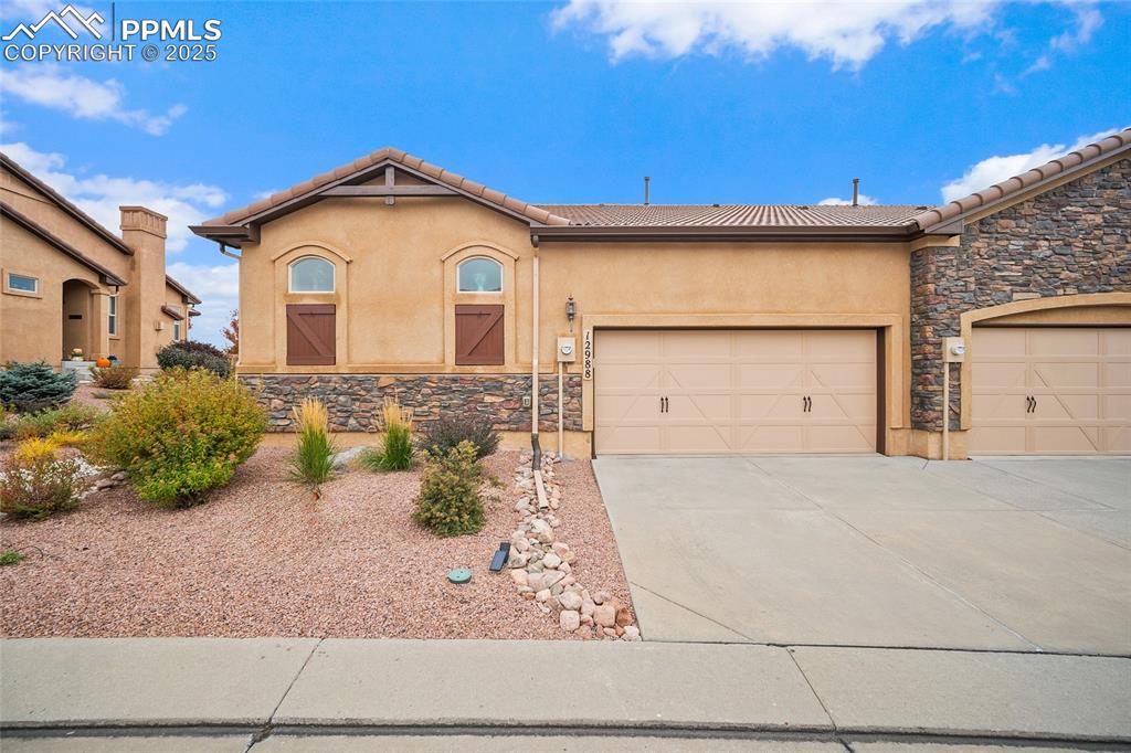 Image 3 of 39: View of front of house with stucco siding, stone siding, concrete driveway,