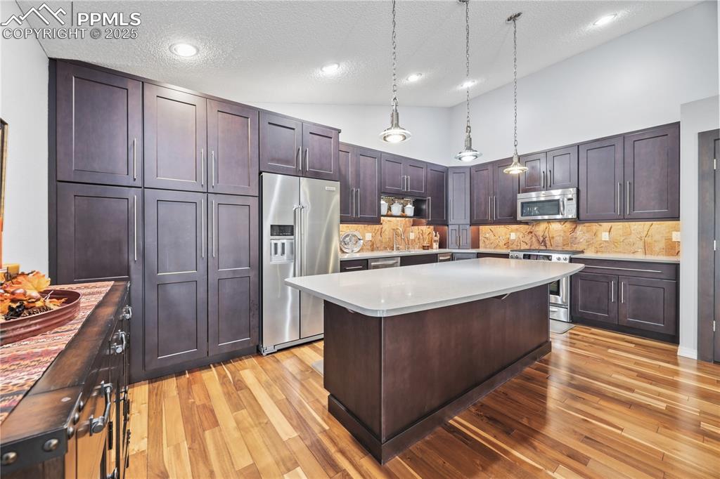 Image 16 of 50: Kitchen featuring dark brown cabinetry, stainless steel appliances, pendant