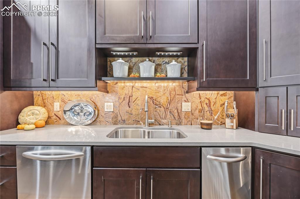 Image 18 of 50: Kitchen featuring stainless steel dishwasher, dark brown cabinetry, light s