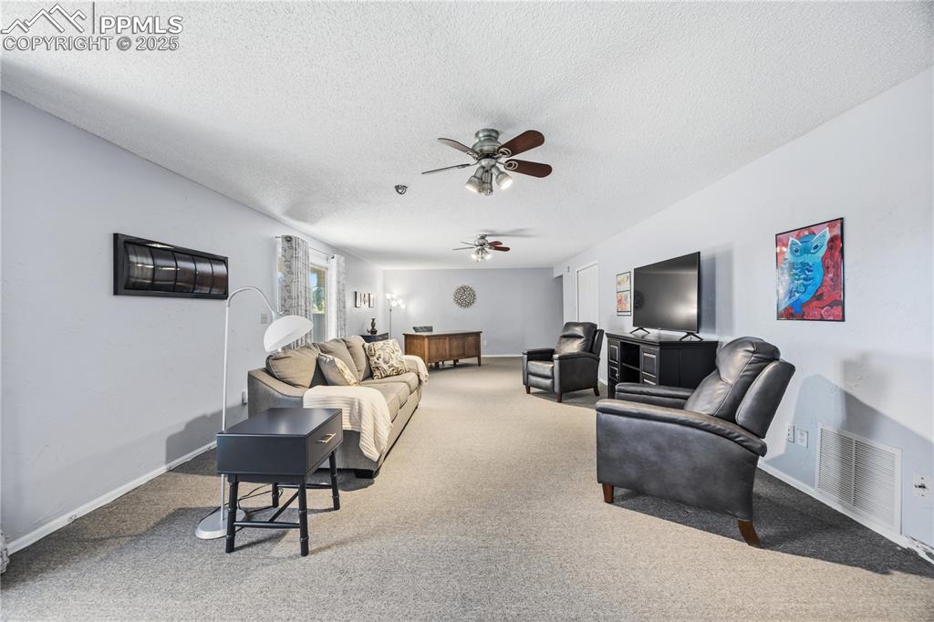 Image 37 of 50: Living area with a textured ceiling, carpet flooring, and a ceiling fan