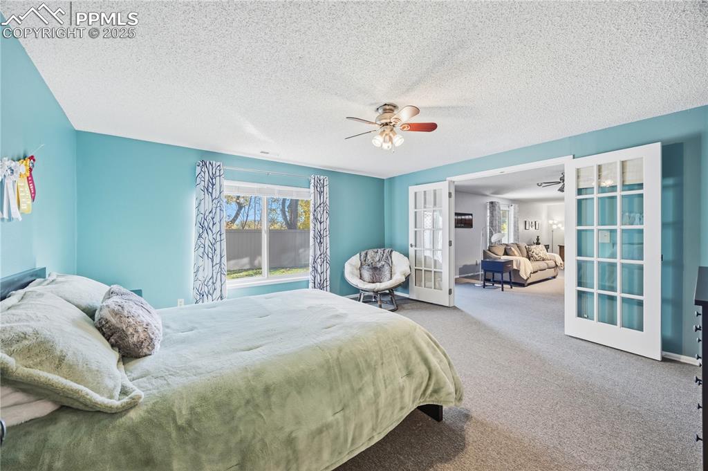 Image 40 of 50: Bedroom with french doors, carpet floors, a textured ceiling, and ceiling f