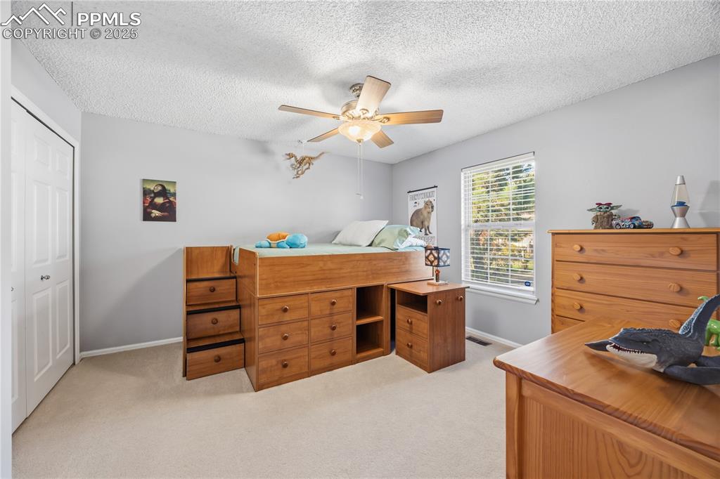 Image 6 of 50: Bedroom featuring light carpet, a closet, a textured ceiling, a ceiling fan