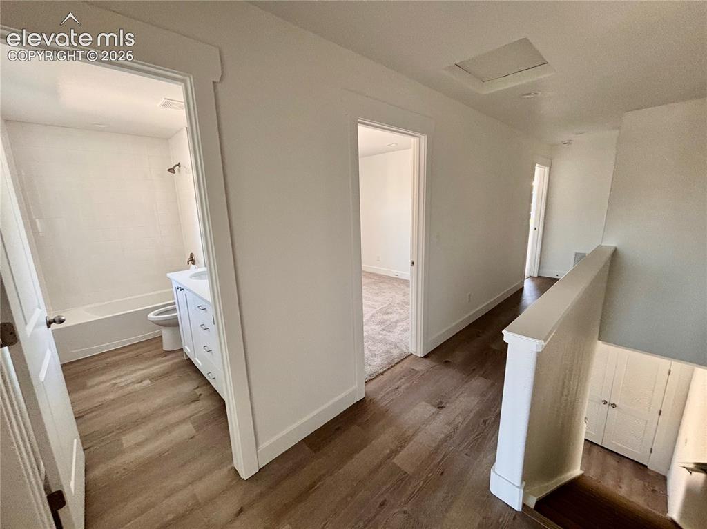 Image 7 of 17: Hallway featuring warm wood-finish flooring, white painted walls, and multi