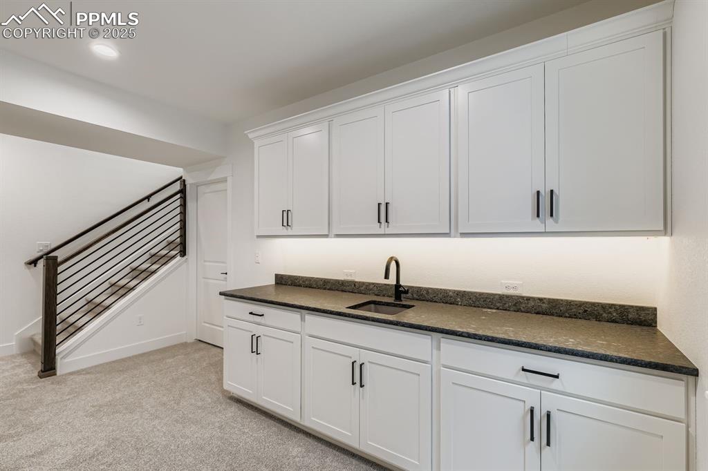 Image 21 of 28: Kitchen featuring white cabinetry, light carpet, and dark stone counters