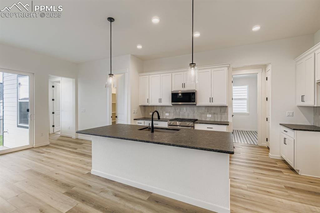 Image 7 of 28: Kitchen with white cabinetry, stainless steel appliances, decorative backsp