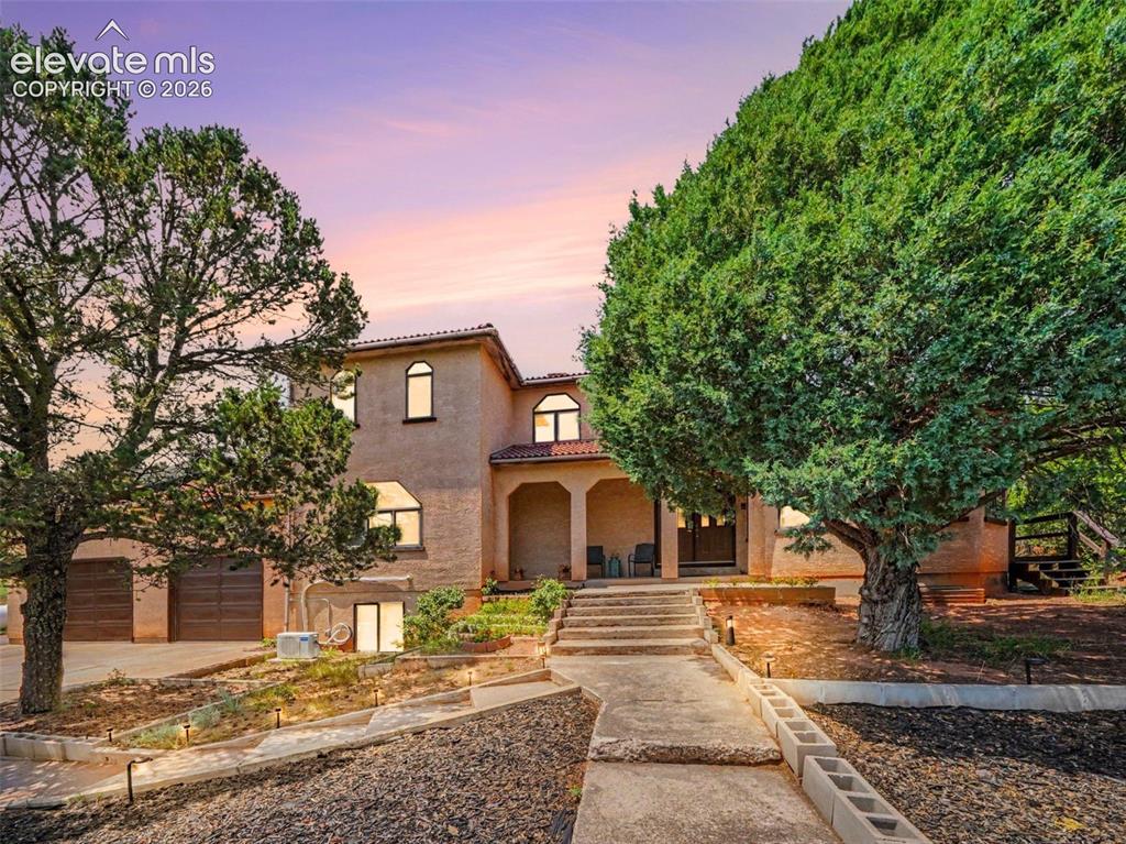 Caption: The stucco front exterior is framed by mature trees and natural landscaping, creating a welcoming en