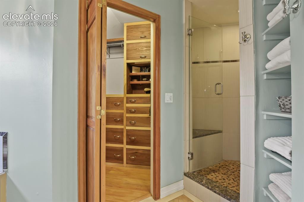 Image 23 of 41: Primary bath with walk-in shower and custom walk-in closet featuring built-