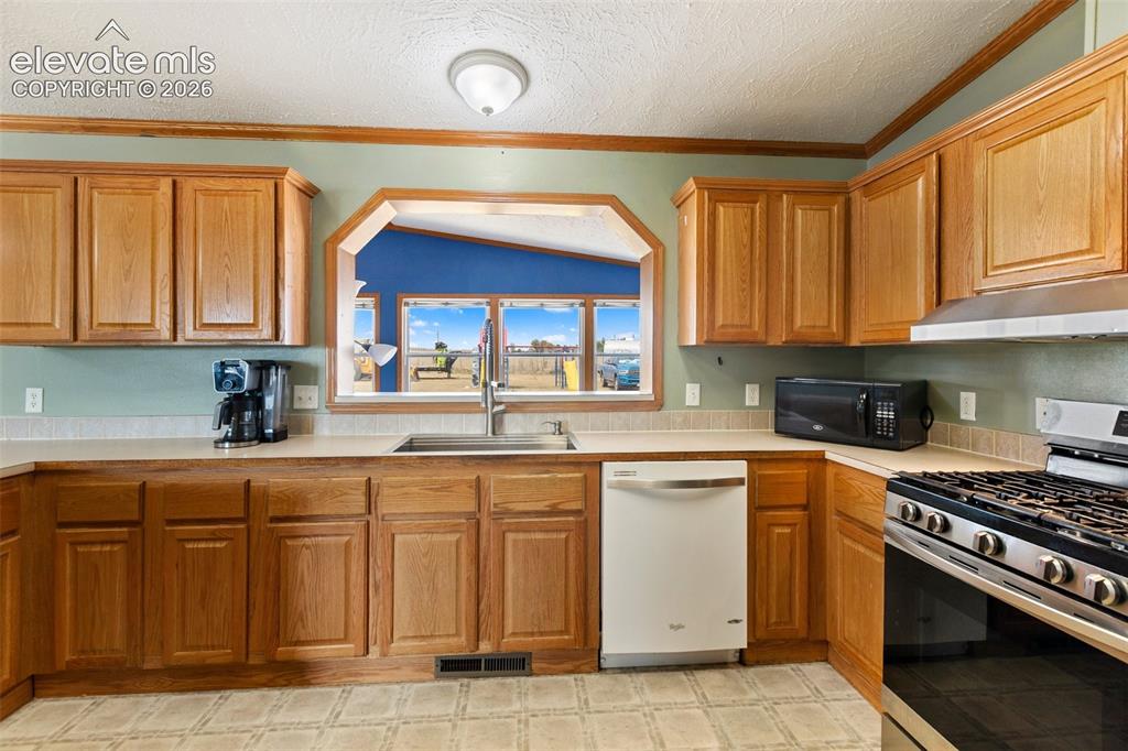 Image 25 of 45: Kitchen featuring wood cabinetry, light countertops, a stainless steel gas