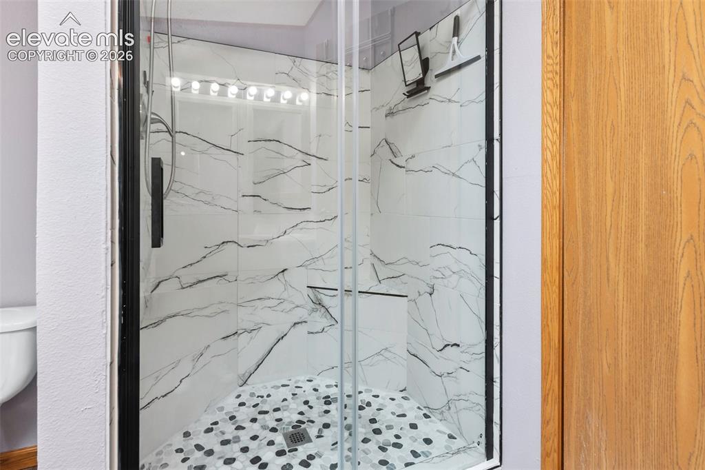 Image 32 of 45: Walk-in shower featuring clear glass enclosure with dark trim, marble-patte