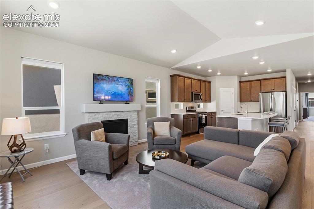 Image 12 of 41: Open-concept living area featuring wood-finish flooring, a stone-faced fire