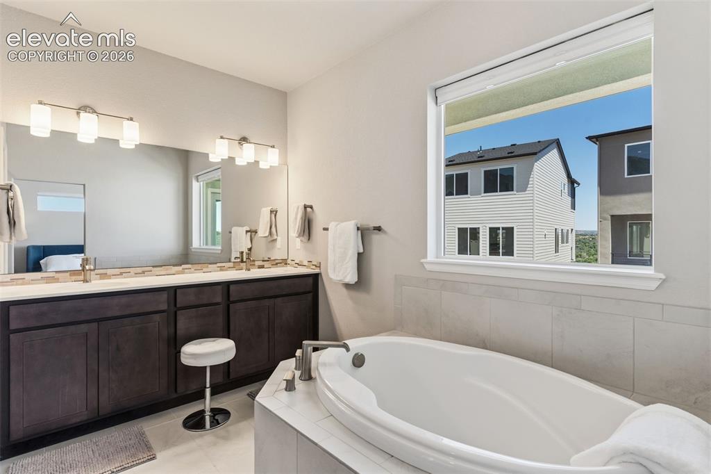 Image 26 of 41: Soaking tub with tile surround, large window, dual vanity with undermount s