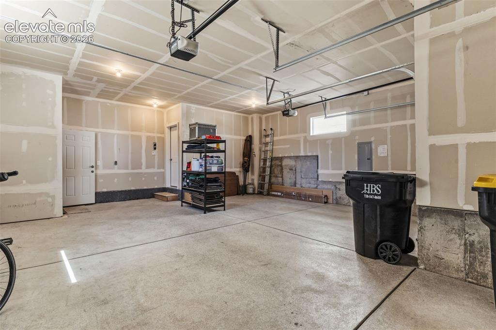 Image 36 of 41: Concrete flooring garage with exposed drywall, featuring two garage door op