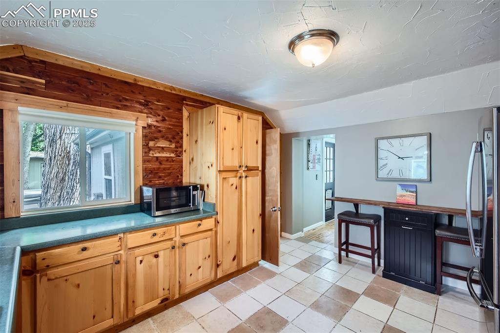 Image 12 of 20: Kitchen with stainless steel microwave, freestanding refrigerator, a desk, 