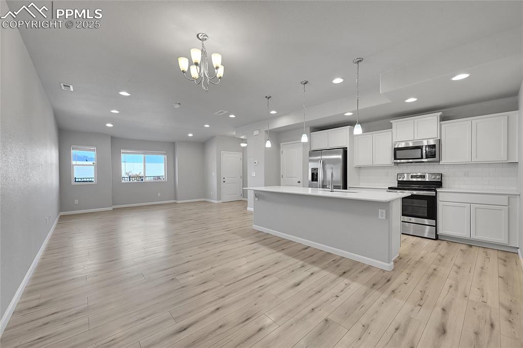Image 12 of 46: Kitchen with decorative light fixtures, tasteful backsplash, white cabinets