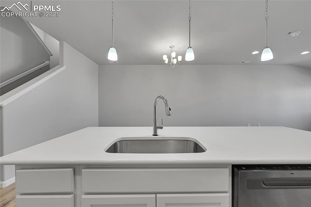 Image 17 of 46: Kitchen with dishwasher, pendant lighting, white cabinetry, light stone cou