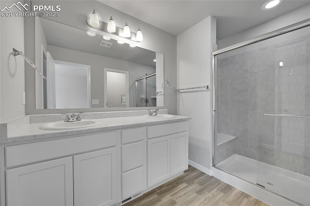 Image 26 of 46: Bathroom featuring double vanity, a shower stall, and light wood-type floor