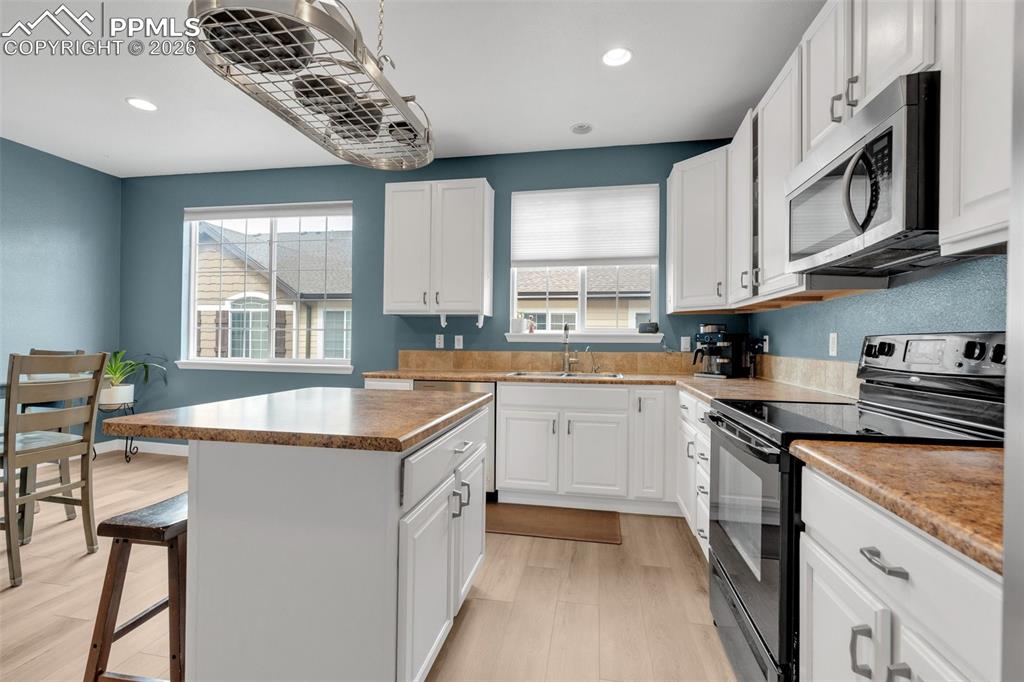 Image 14 of 39: Kitchen featuring stainless steel appliances, a breakfast bar, white cabine