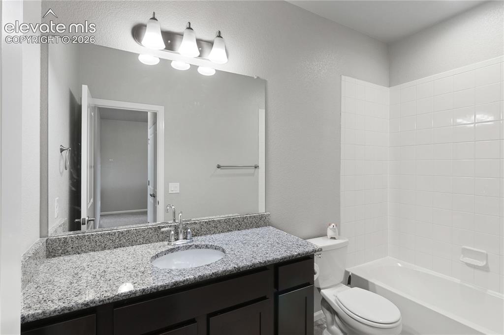 Image 11 of 19: Bathroom featuring a dark wood-finish vanity with a granite countertop, und