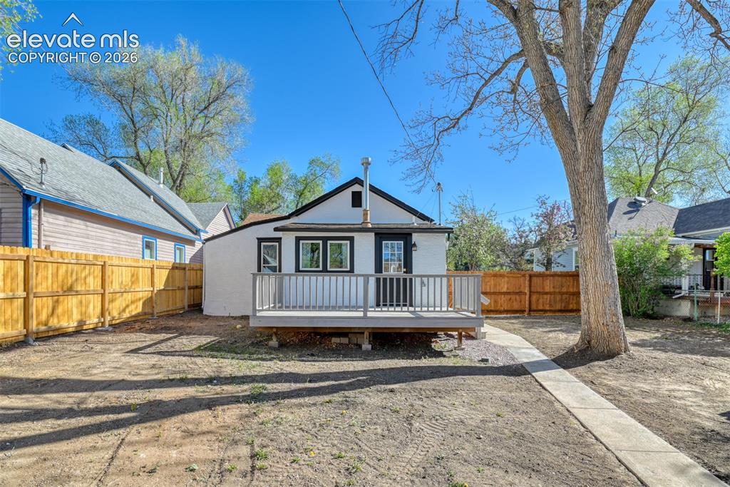 Image 39 of 47: Rear exterior featuring a raised deck, concrete walkway, and wood fencing