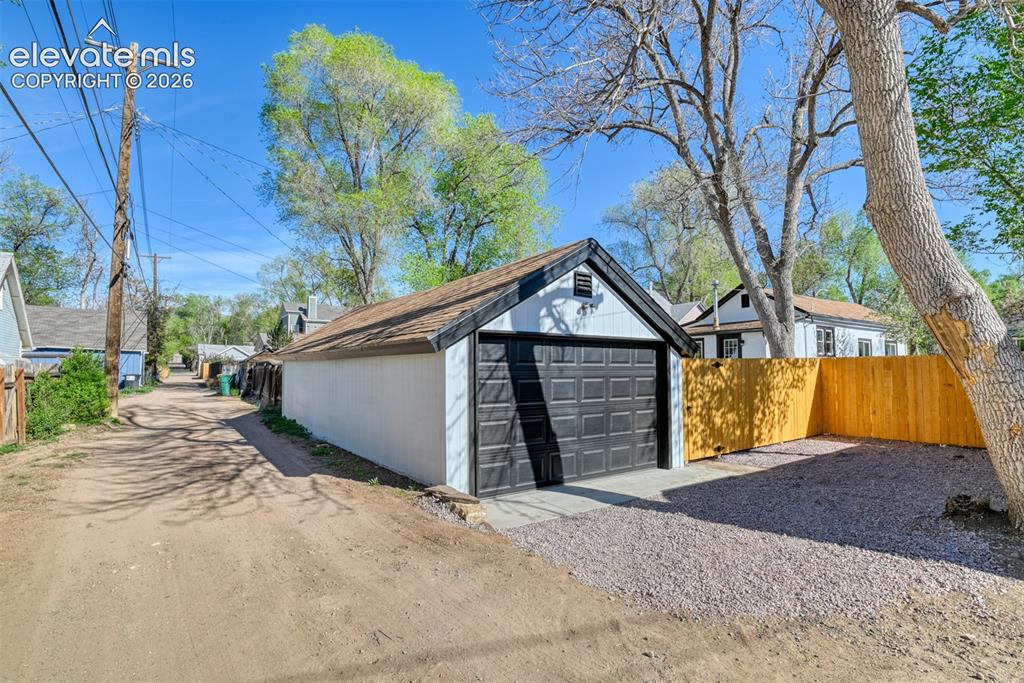 Image 46 of 47: Detached garage with a dark panel-style door and gravel driveway