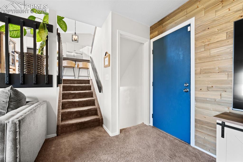 Image 23 of 50: Entryway featuring a striking blue door, a wood accent wall, and carpeted s