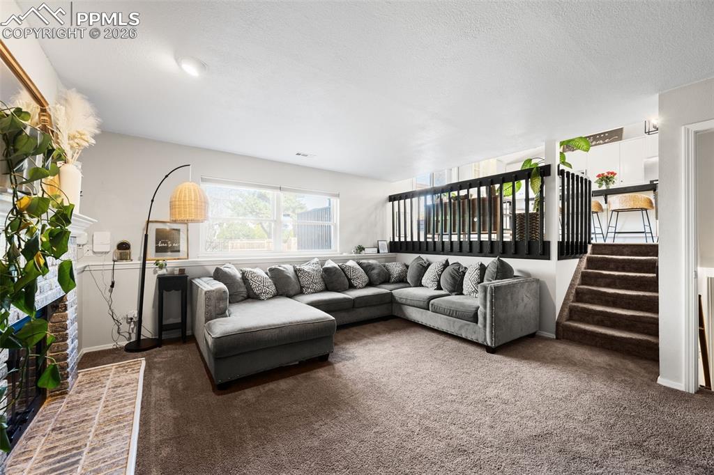 Image 7 of 50: Living area featuring carpeted floors, a large window, and a brick fireplac