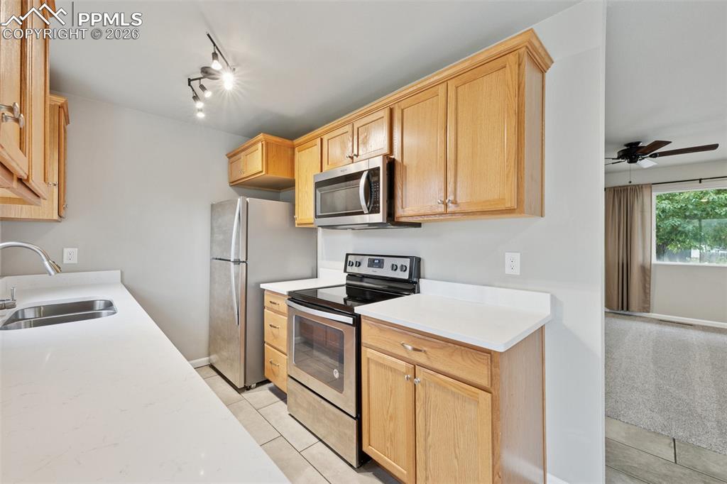 Image 3 of 34: Kitchen with stainless steel appliances, ceiling fan, light stone counters,