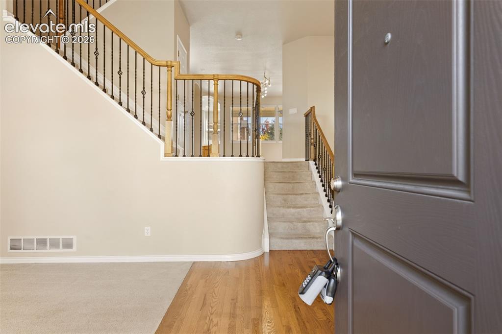 Image 11 of 44: Entryway with a two-story staircase featuring wrought iron balusters and wo