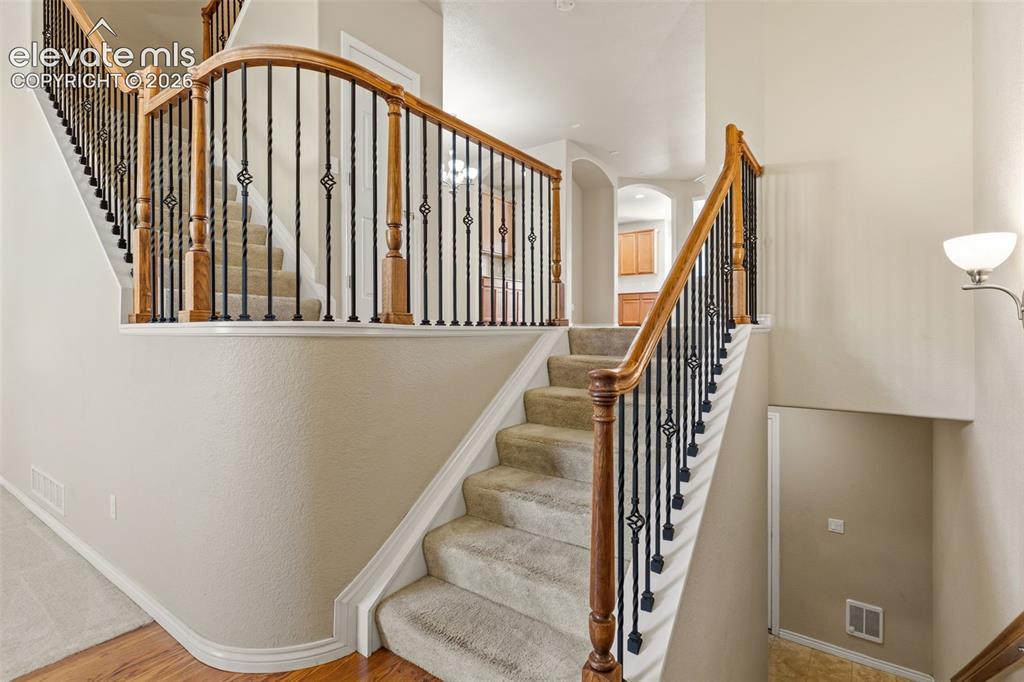 Image 16 of 44: Staircase featuring wood handrails, wrought iron balusters, and carpeted tr