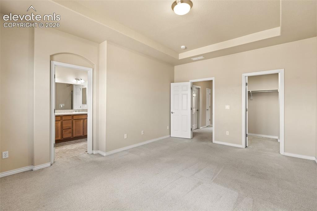 Image 33 of 44: Neutral-toned carpeting and walls, tray ceiling, and a large open doorway l