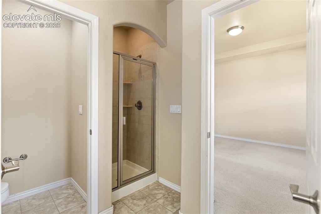 Image 36 of 44: Glass-enclosed shower with a bronze-finish showerhead, tiled shower surroun