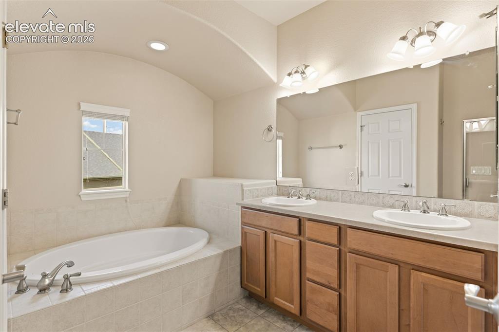 Image 37 of 44: Dual vanity with wood-finish cabinetry, built-in soaking tub, tile surround