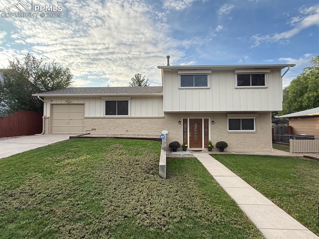 Caption: Tri-level home with brick siding, an attached garage, concrete driveway, board and batten siding, an