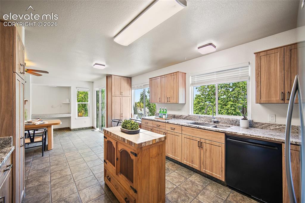Image 15 of 45: Kitchen featuring wood-finish cabinetry, stone-look countertops, and tile f