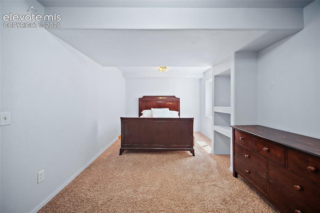 Image 32 of 45: Carpeted room with recessed wall shelving, white painted walls, and a ceili