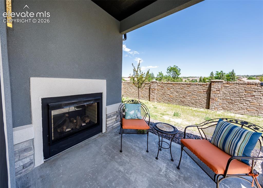 Image 19 of 50: Covered patio with a built-in outdoor fireplace, stucco exterior, and stone