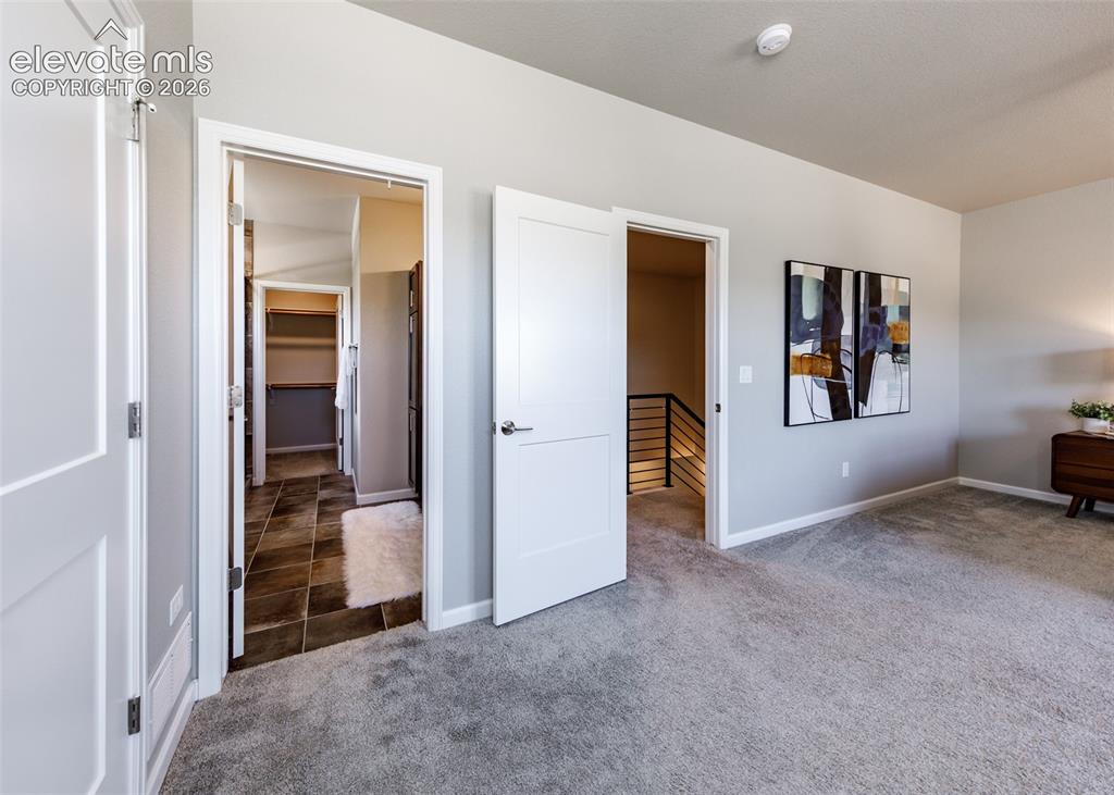 Image 32 of 50: Carpeted room with light grey walls, two panel interior doors, and white ba
