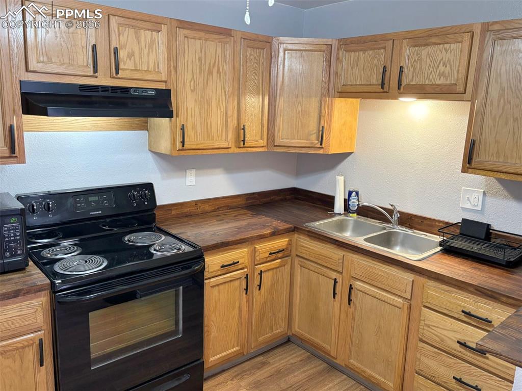 Image 13 of 17: Kitchen with black appliances, wood counters, a textured wall, and light wo