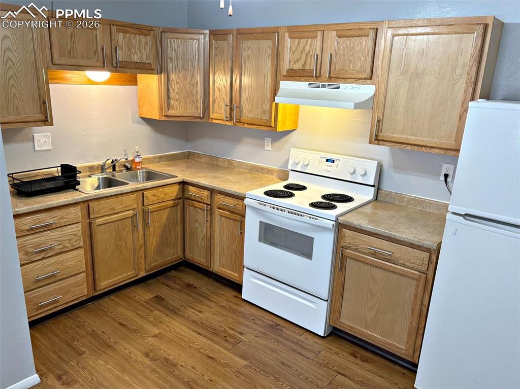 Image 6 of 17: Kitchen featuring white appliances, light countertops, and dark wood-style